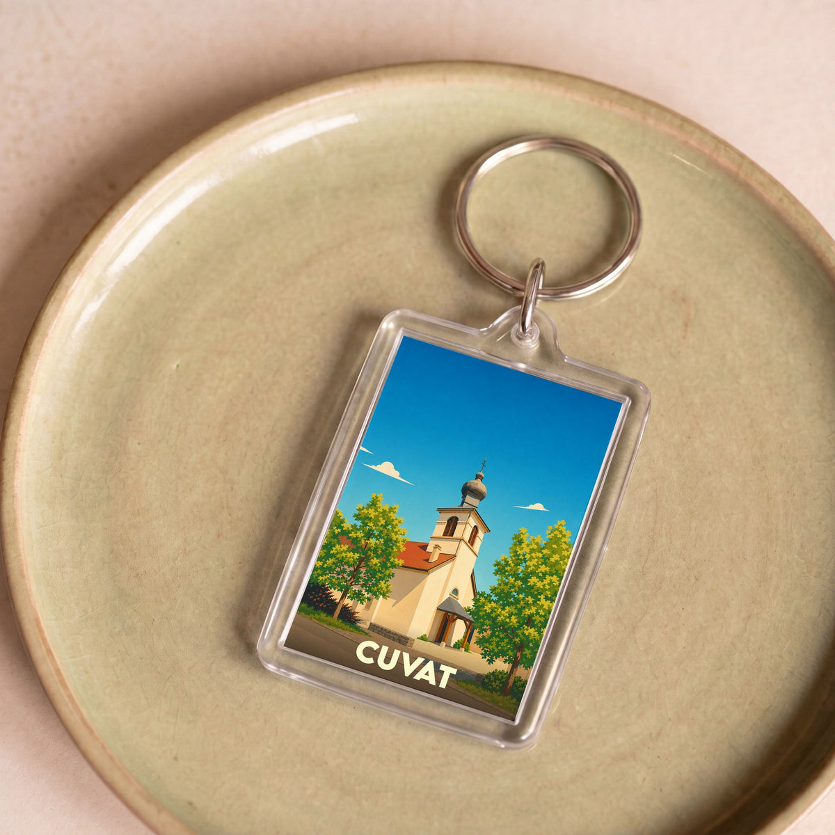 Porte-clés souvenir de la ville de Cuvat illustré d'une église pittoresque sous un ciel bleu.