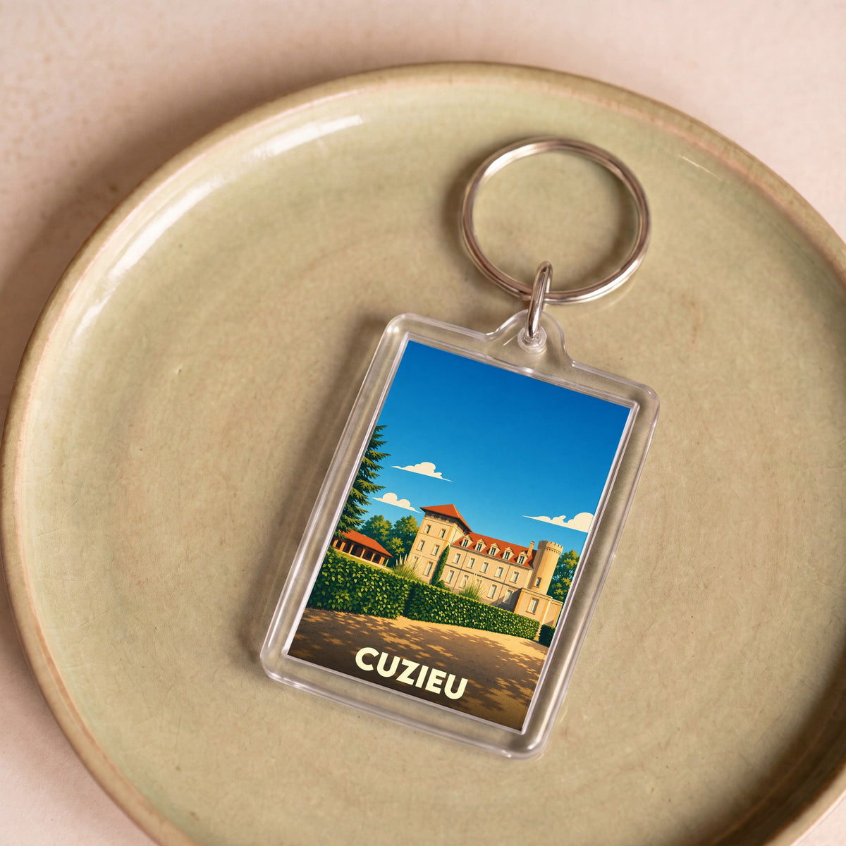 Porte-clés souvenir de la ville de Cuzieu avec une illustration stylisée d'un château sous un ciel bleu.