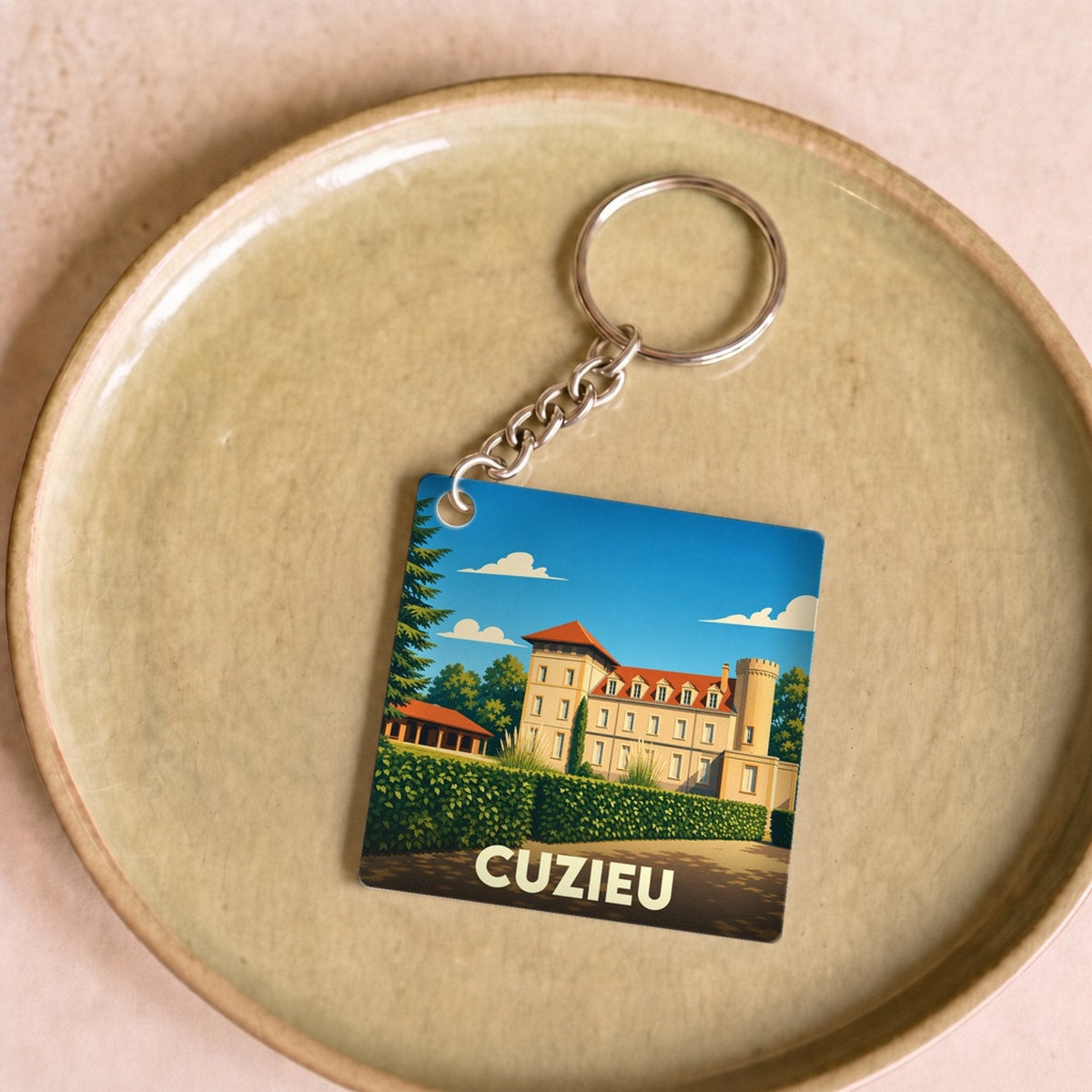 Porte-clés souvenir de la ville de Cuzieu avec une illustration stylisée d'un château sous un ciel bleu.