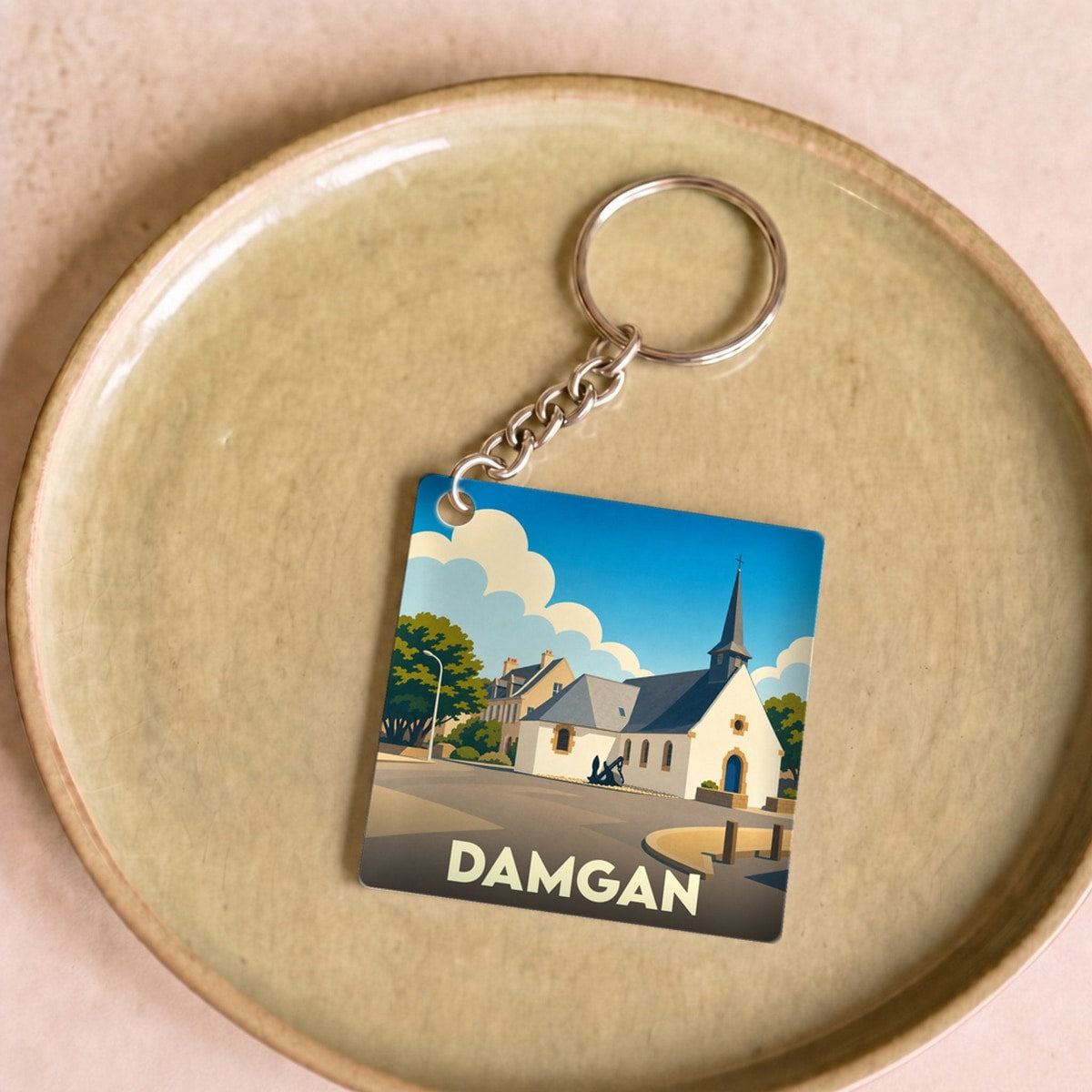 Porte-clés souvenir de la ville de Damgan avec une illustration stylisée de son église sous un ciel bleu.