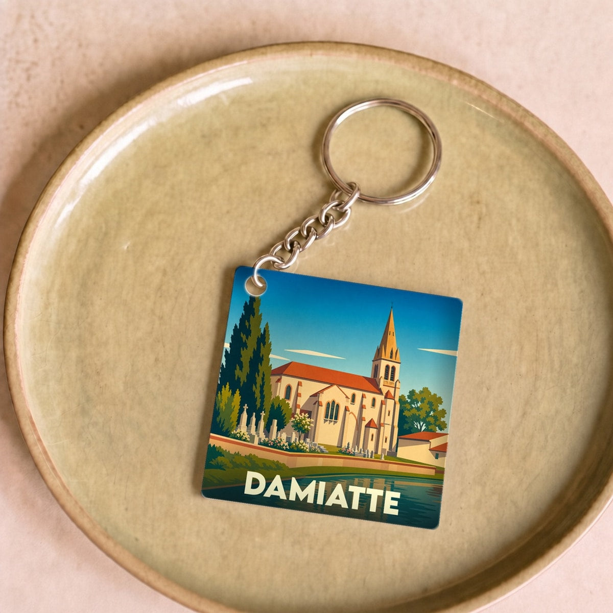 Porte-clés souvenir de la ville de Damiatte avec une illustration stylisée de son église au bord de l'eau.
