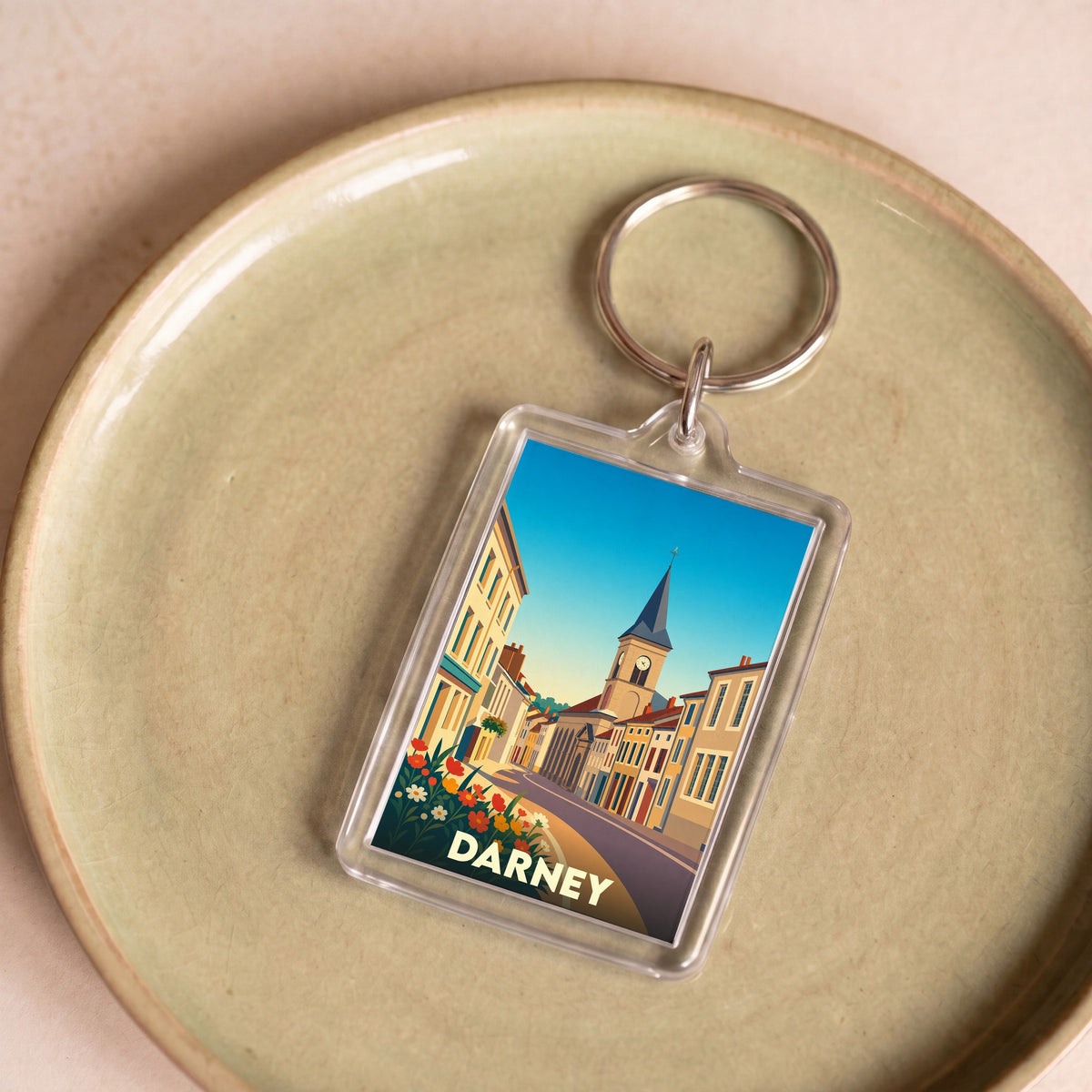 Porte-clés souvenir de la ville de Darney avec une illustration stylisée d'une rue historique.