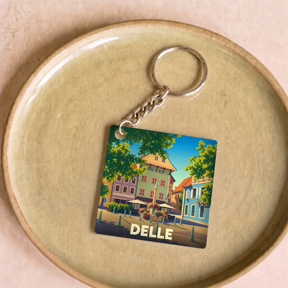 Porte-clés souvenir de la ville de Delle avec une illustration stylisée d'une place colorée.