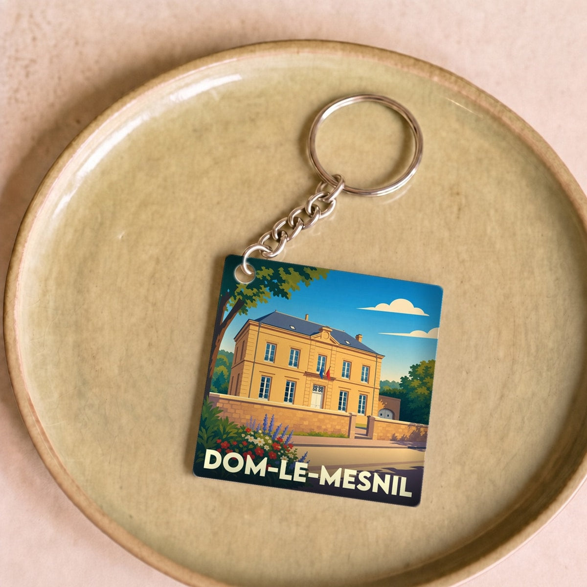 Porte-clés souvenir de la ville de Dom-le-Mesnil avec une illustration stylisée de sa mairie.