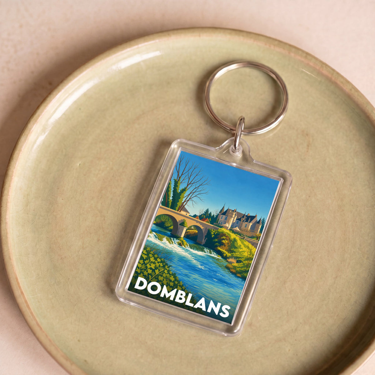 Porte-clés souvenir de la ville de Domblans avec une illustration stylisée d'un paysage local.