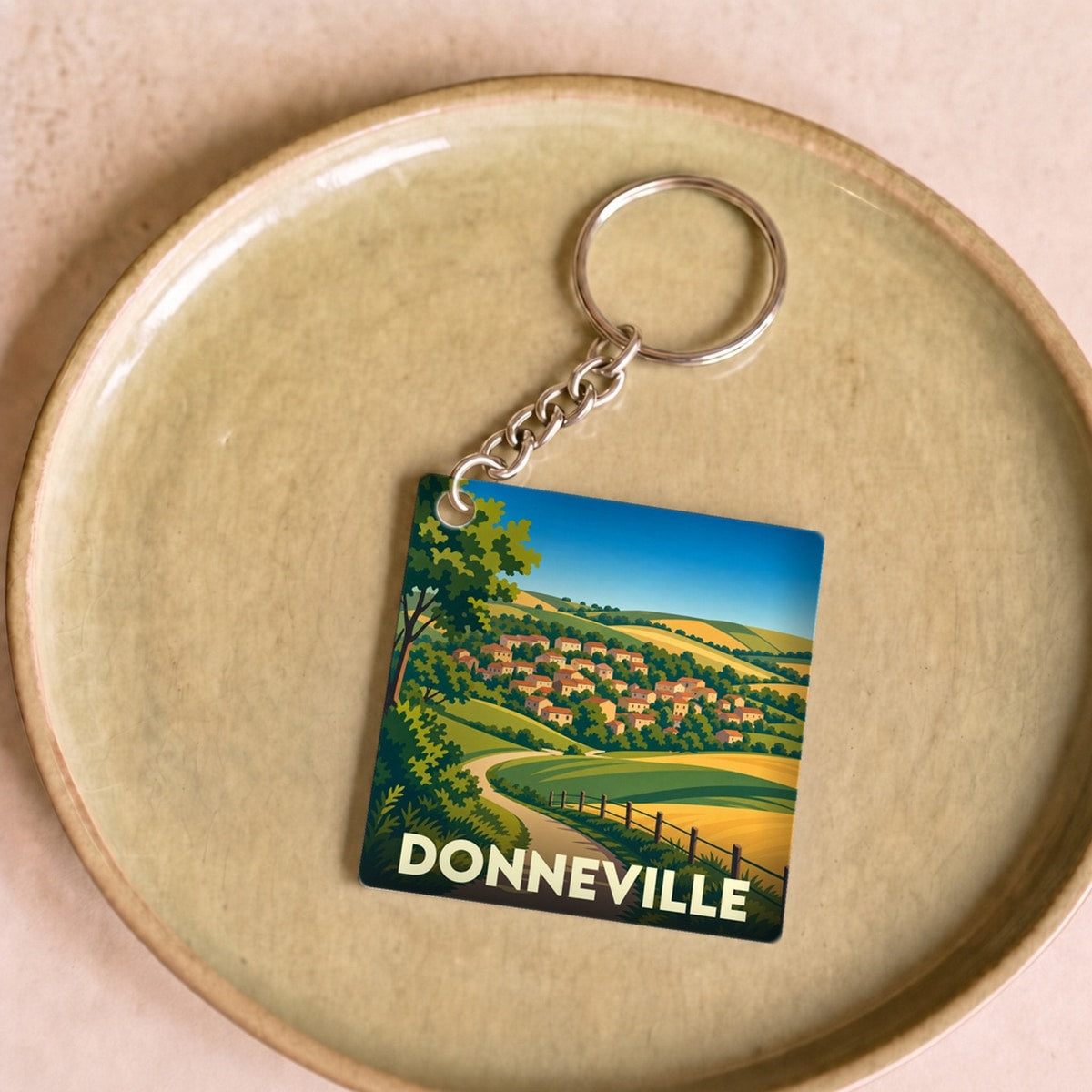 Porte-clés souvenir de la ville de Donneville avec une illustration stylisée de son paysage vallonné.