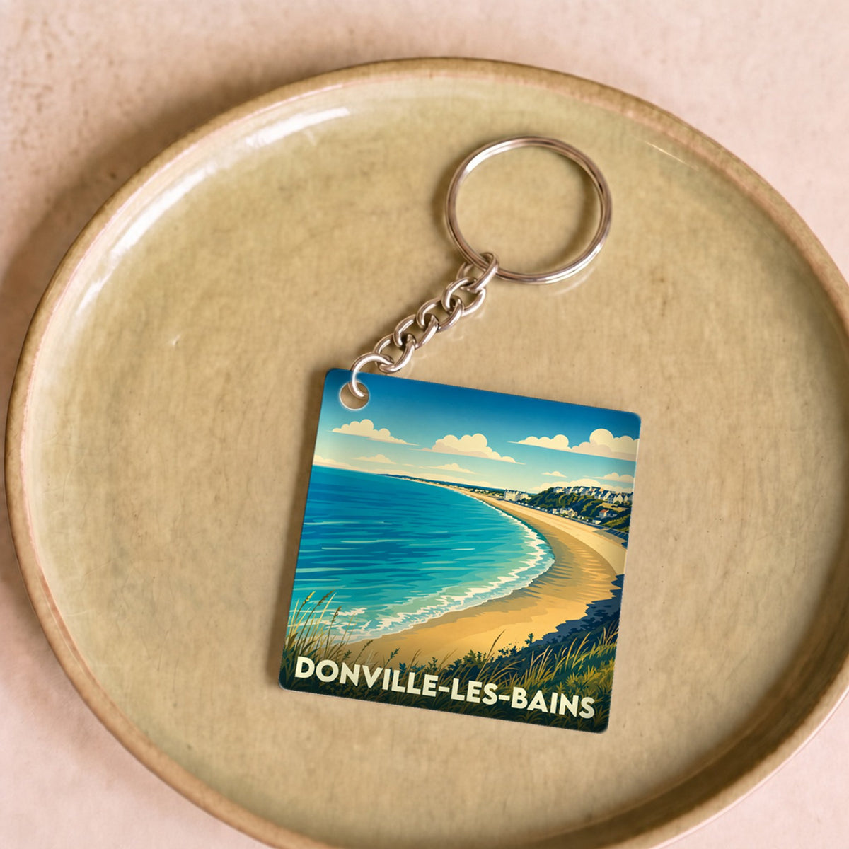 Porte-clés souvenir de la ville de Donville-les-Bains avec une illustration stylisée de sa plage.