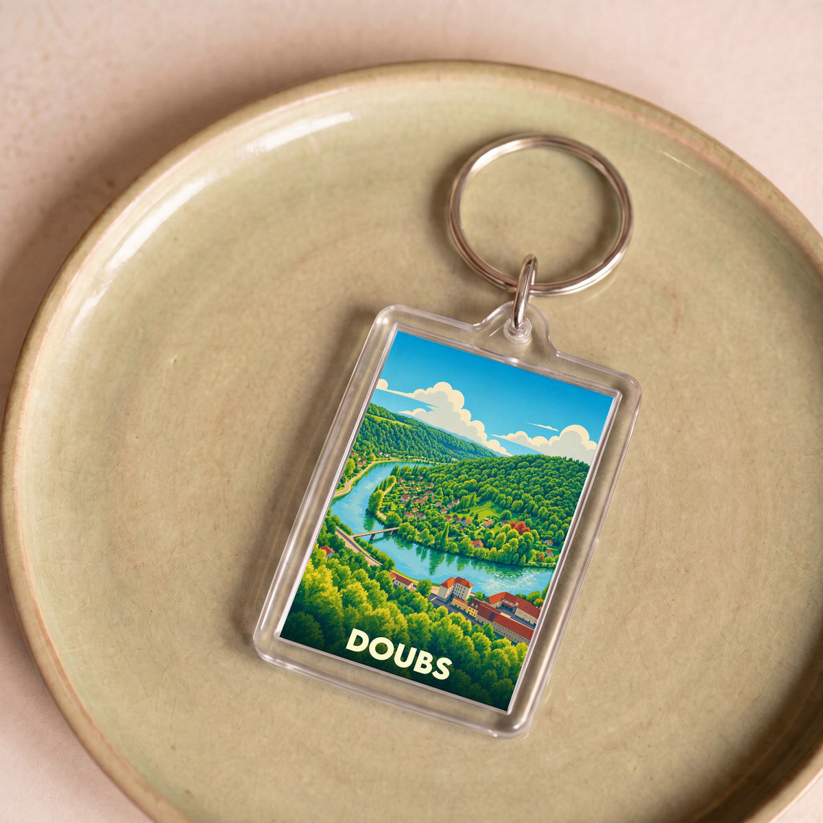 Porte-clés souvenir du département du Doubs avec une illustration stylisée d'un paysage de rivière et de montagnes.