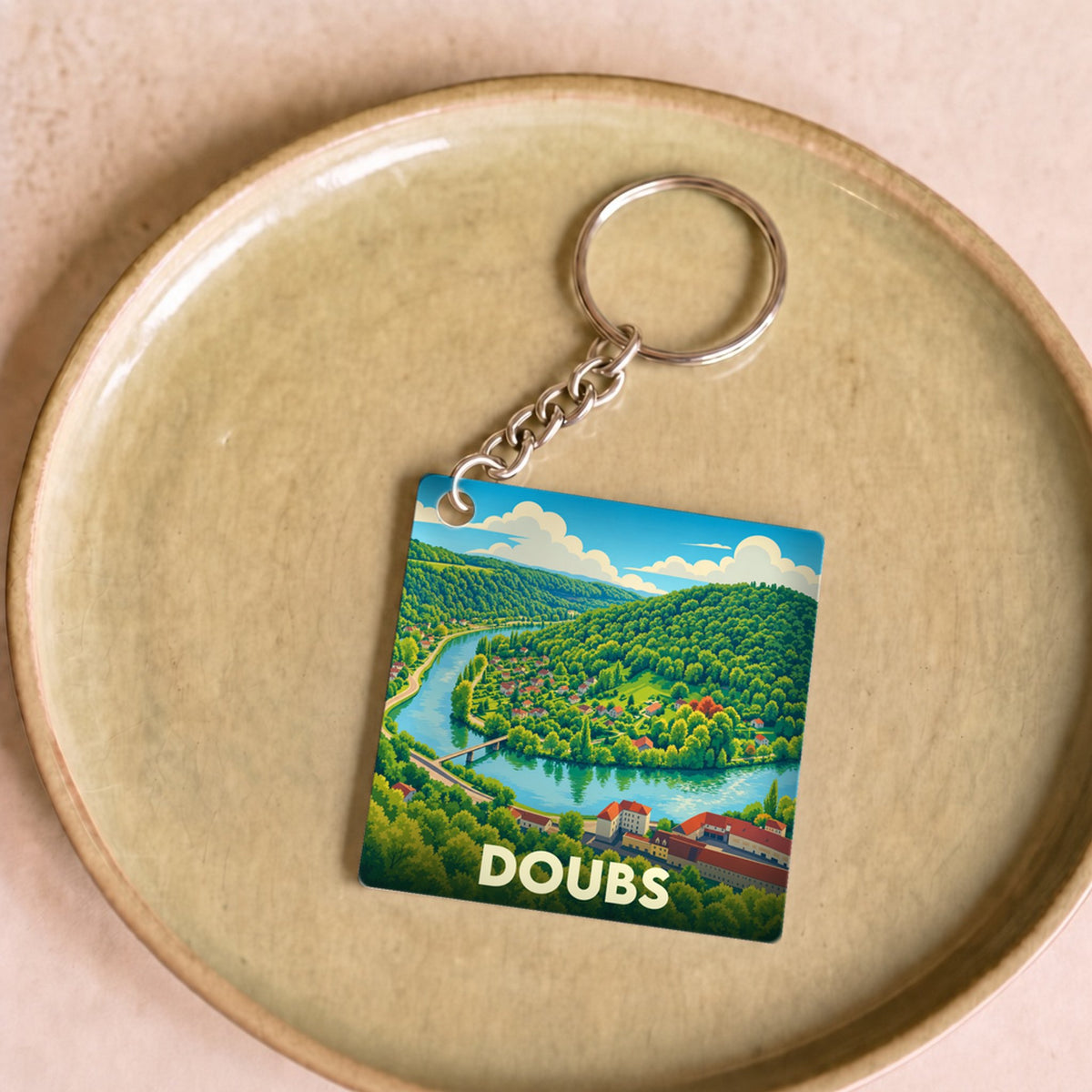 Porte-clés souvenir du département du Doubs avec une illustration stylisée d'un paysage de rivière et de montagnes.