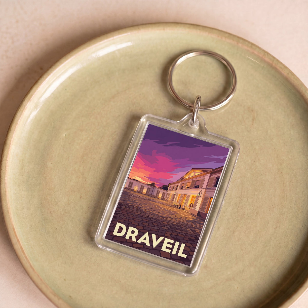 Porte-clés souvenir de la ville de Draveil avec une illustration stylisée d'un bâtiment au coucher du soleil.
