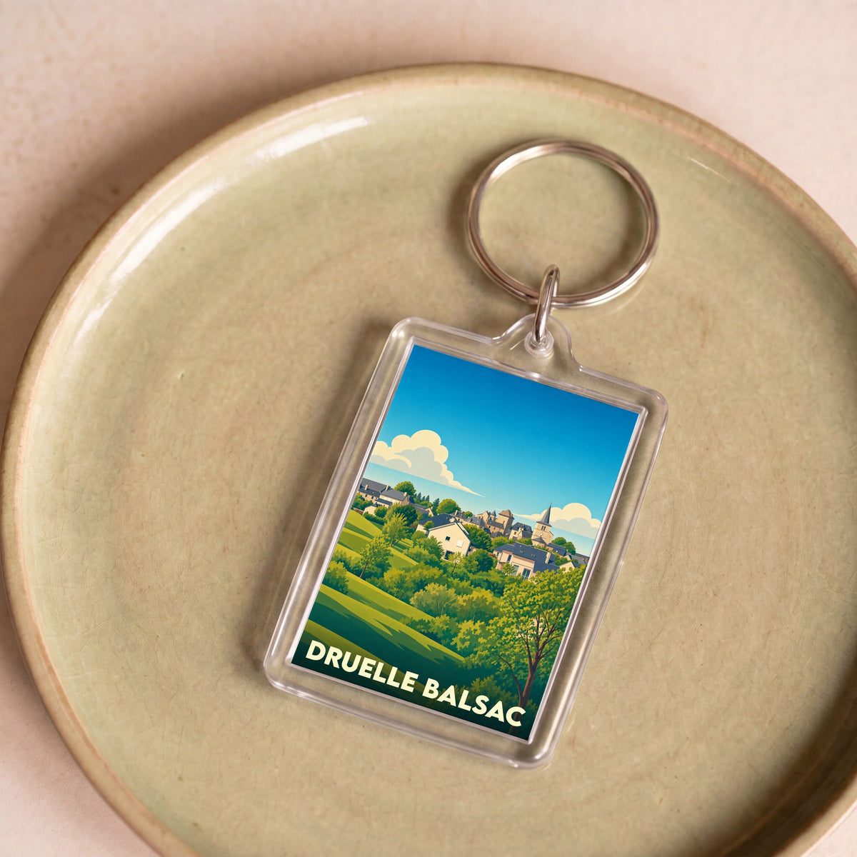 Porte-clés souvenir de la ville de Druelle Balsac avec une illustration stylisée de son paysage.