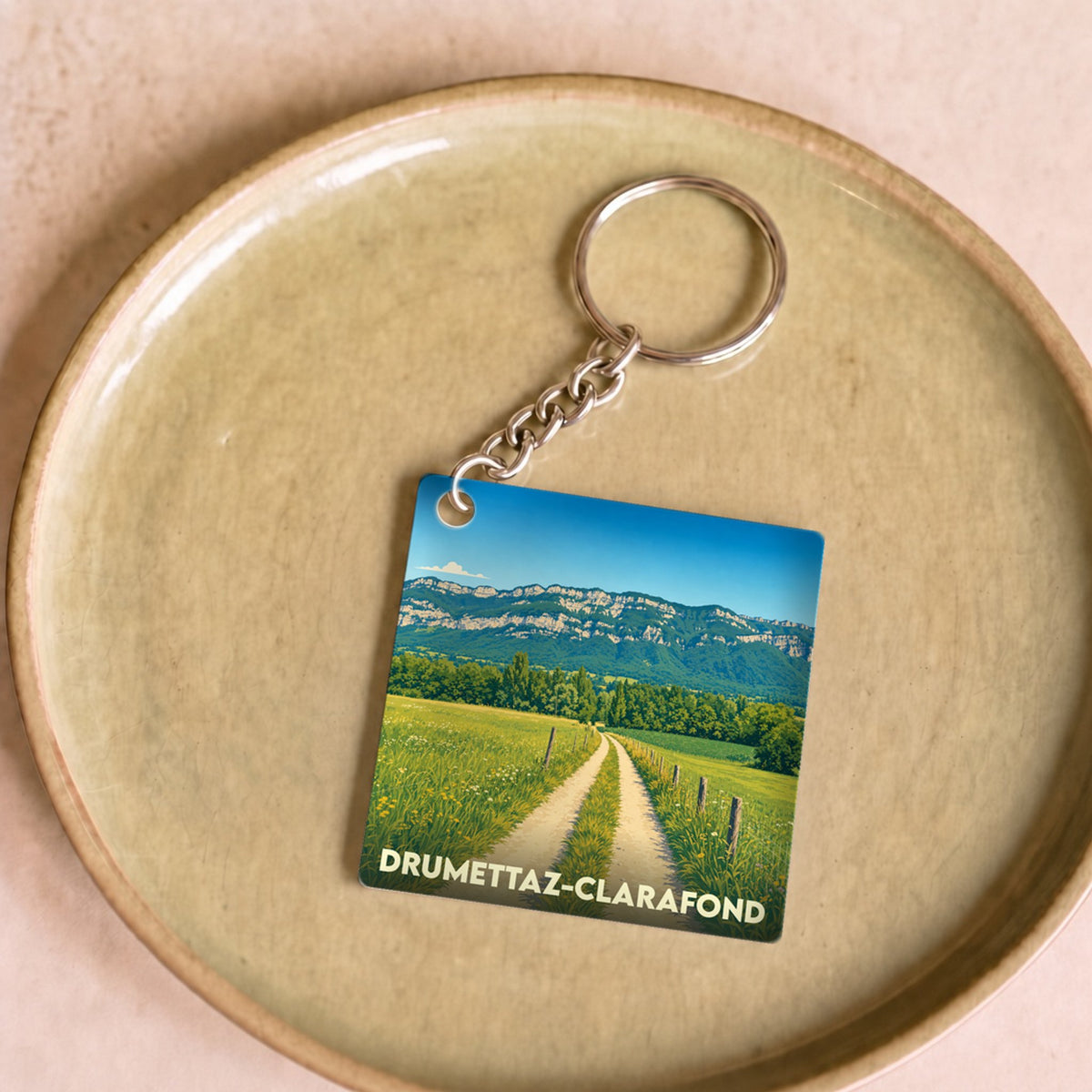 Porte-clés souvenir de la ville de Drumettaz-Clarafond avec une illustration stylisée d'un paysage de campagne.