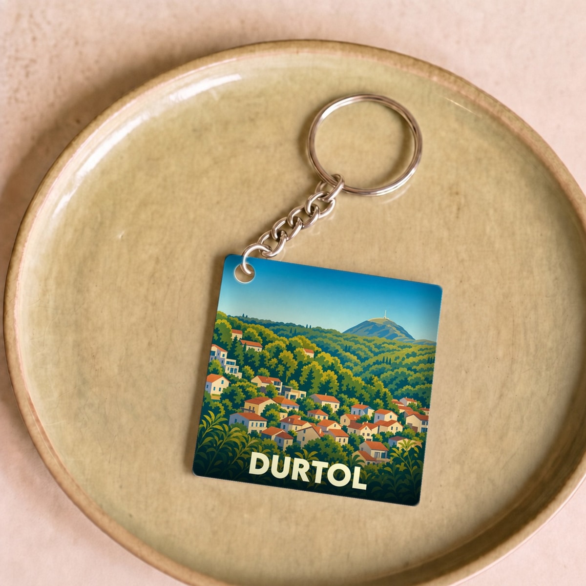 Porte-clés souvenir de la ville de Durtol avec une illustration stylisée de ses maisons flanc de colline.