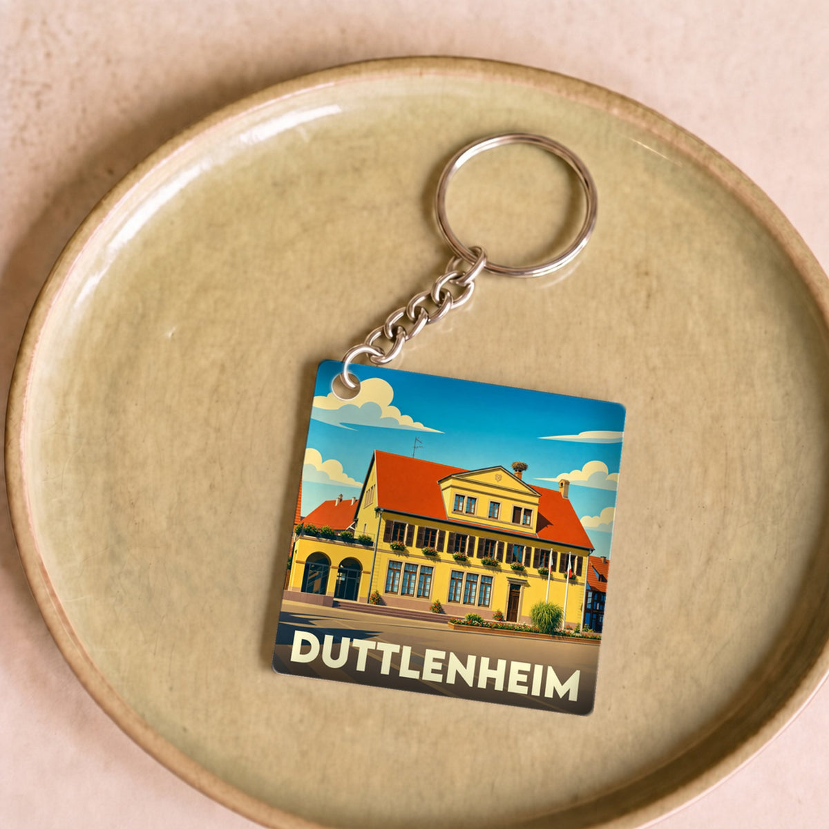 Porte-clés souvenir de la ville de Duttlenheim avec une illustration stylisée d'un bâtiment traditionnel.