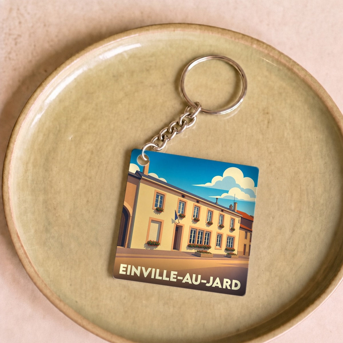 Porte-clés souvenir de la ville de Einville-au-Jard avec une illustration stylisée d'un bâtiment ensoleillé.