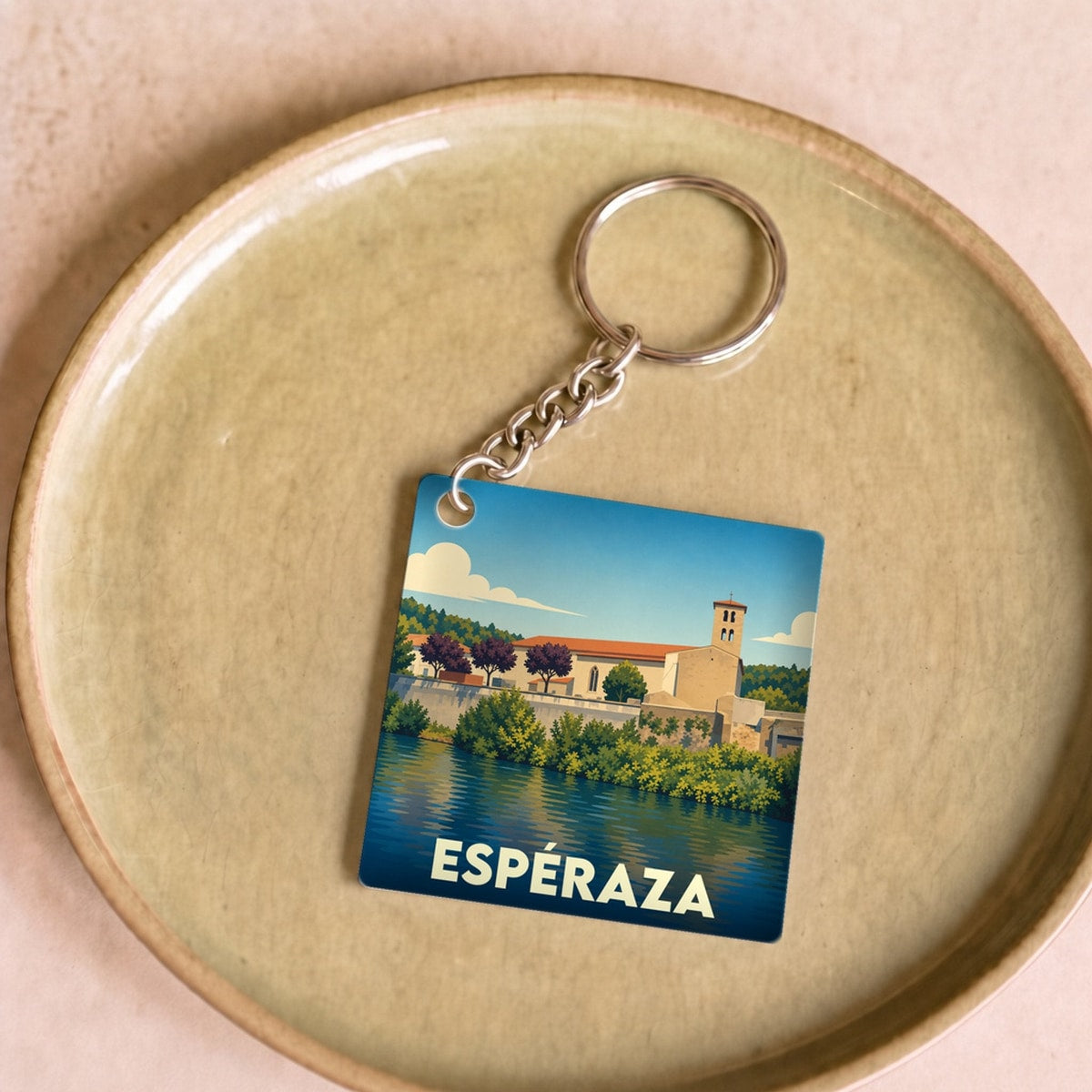 Porte-clés souvenir de la ville d'Espéraza avec une illustration stylisée d'un paysage au bord de l'eau.