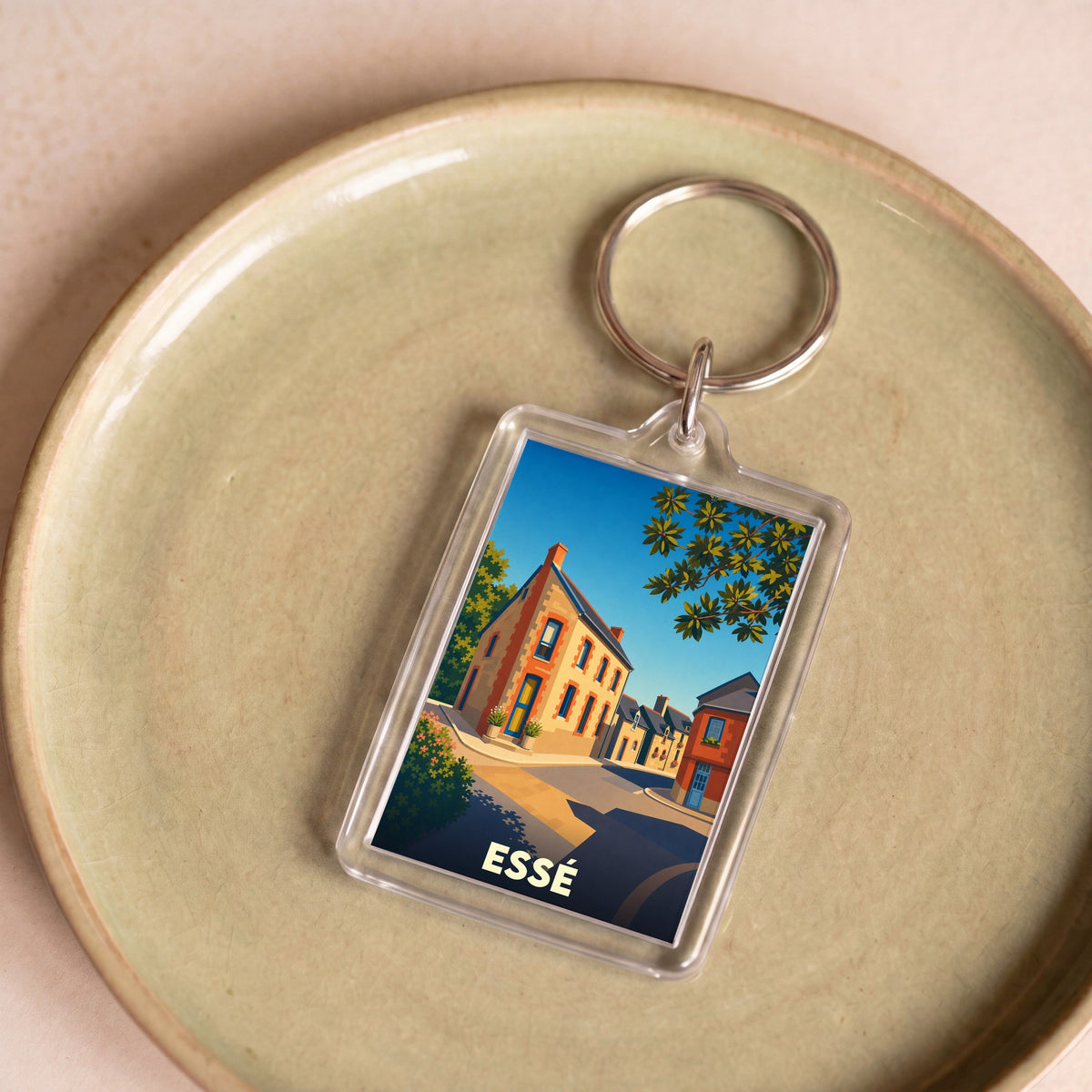 Porte-clés souvenir de la ville d'Essé avec une illustration stylisée d'une rue ensoleillée.