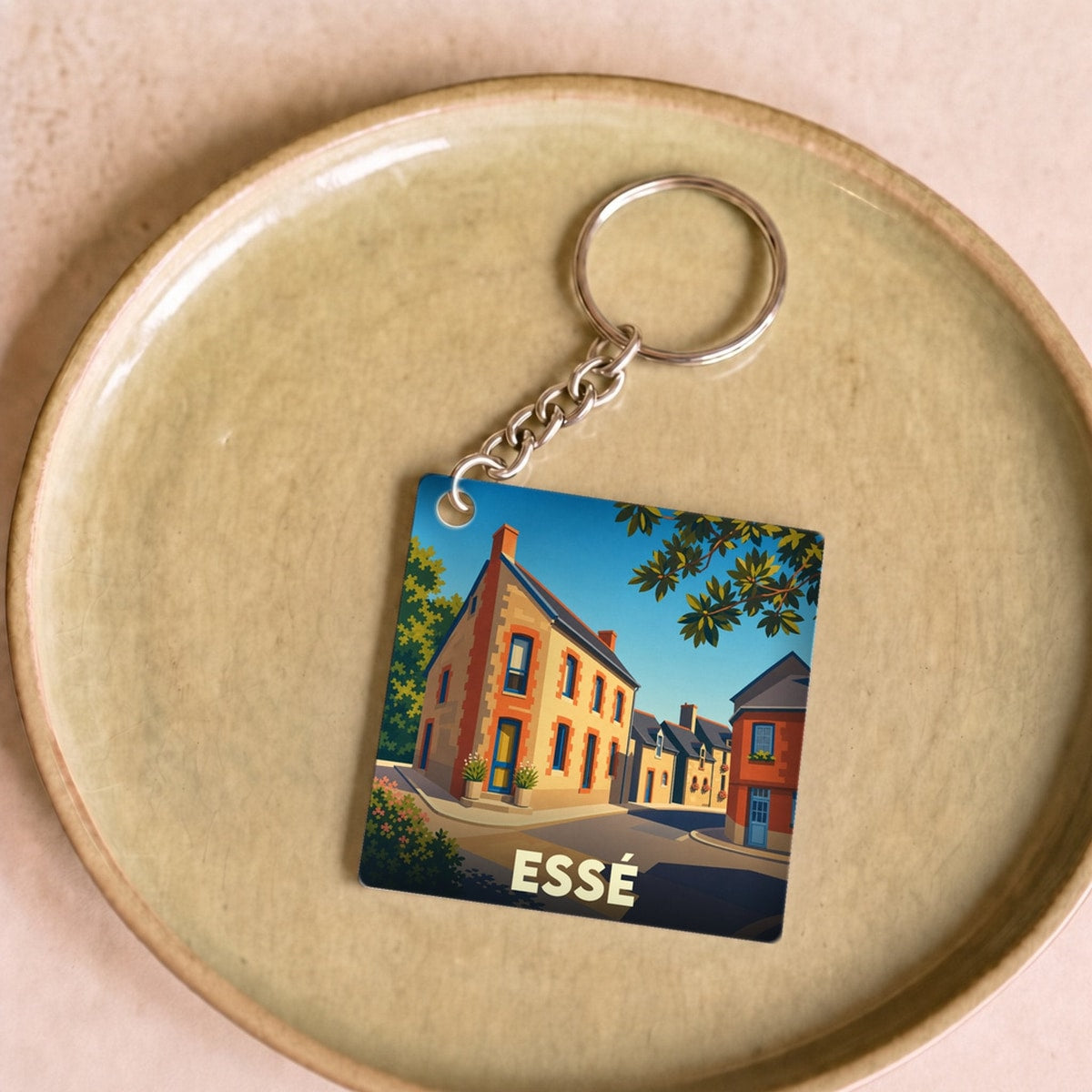 Porte-clés souvenir de la ville d'Essé avec une illustration stylisée d'une rue ensoleillée.