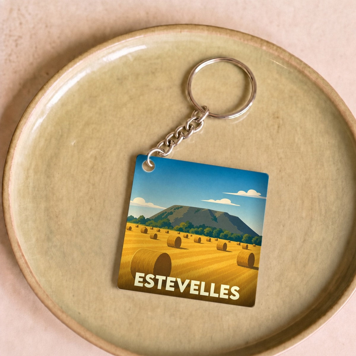 Porte-clés souvenir de la ville d'Estevelles avec une illustration stylisée d'un champ de foin.