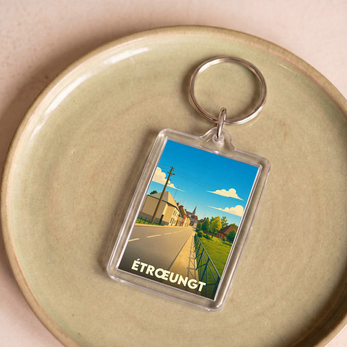 Porte-clés souvenir de la ville de Étrœungt avec une illustration stylisée d'une rue ensoleillée.
