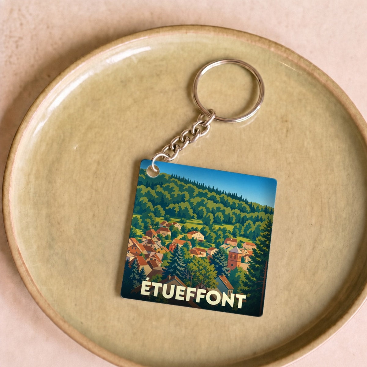 Porte-clés souvenir de la ville de Étueffont avec une illustration stylisée d'un paysage vallonné.