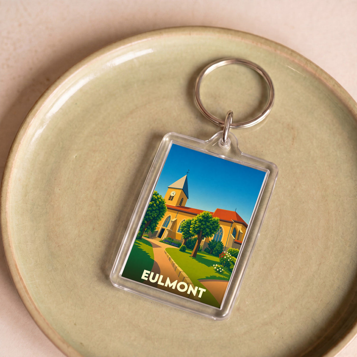 Porte-clés souvenir de la ville d'Eulmont avec une illustration stylisée de son église et d'un jardin.
