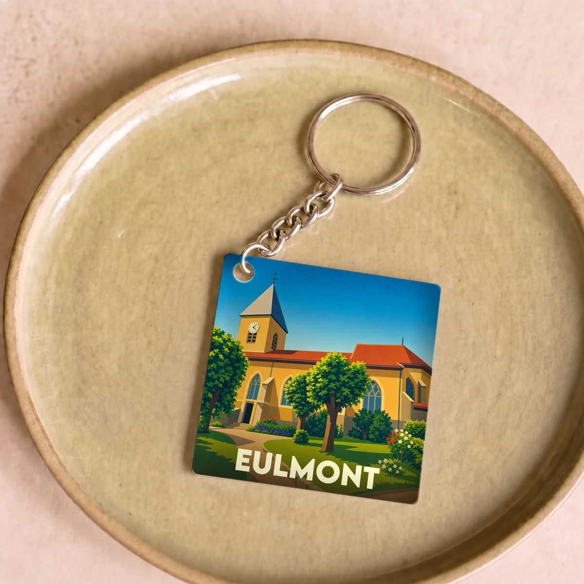 Porte-clés souvenir de la ville d'Eulmont avec une illustration stylisée de son église et d'un jardin.