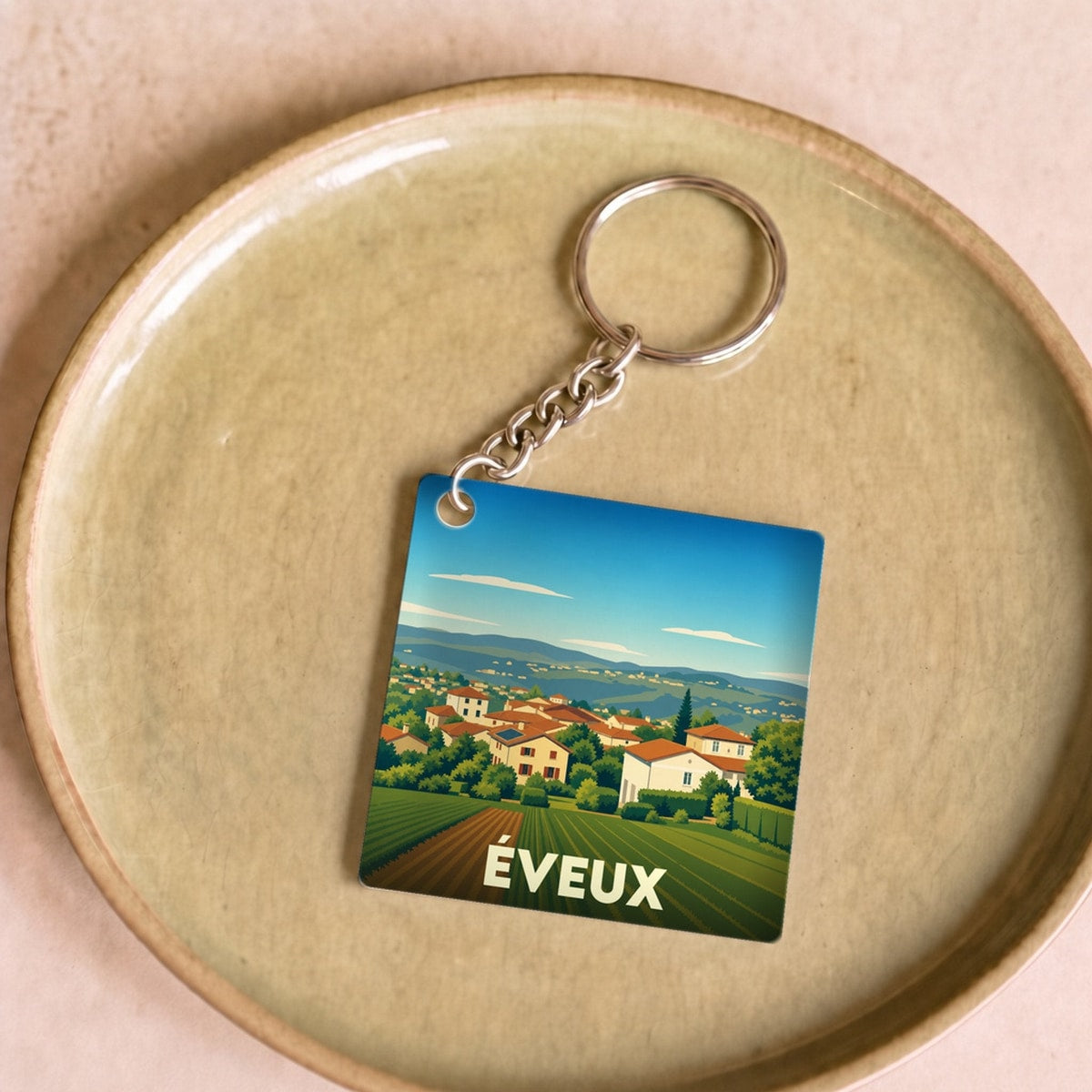 Porte-clés souvenir de la ville de Éveux avec une illustration stylisée de paysages vallonnés.