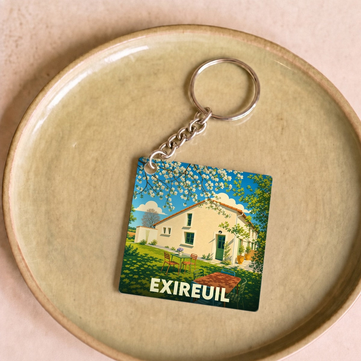Porte-clés souvenir de la ville de Exireuil avec une illustration stylisée d'une maison de campagne ensoleillée.