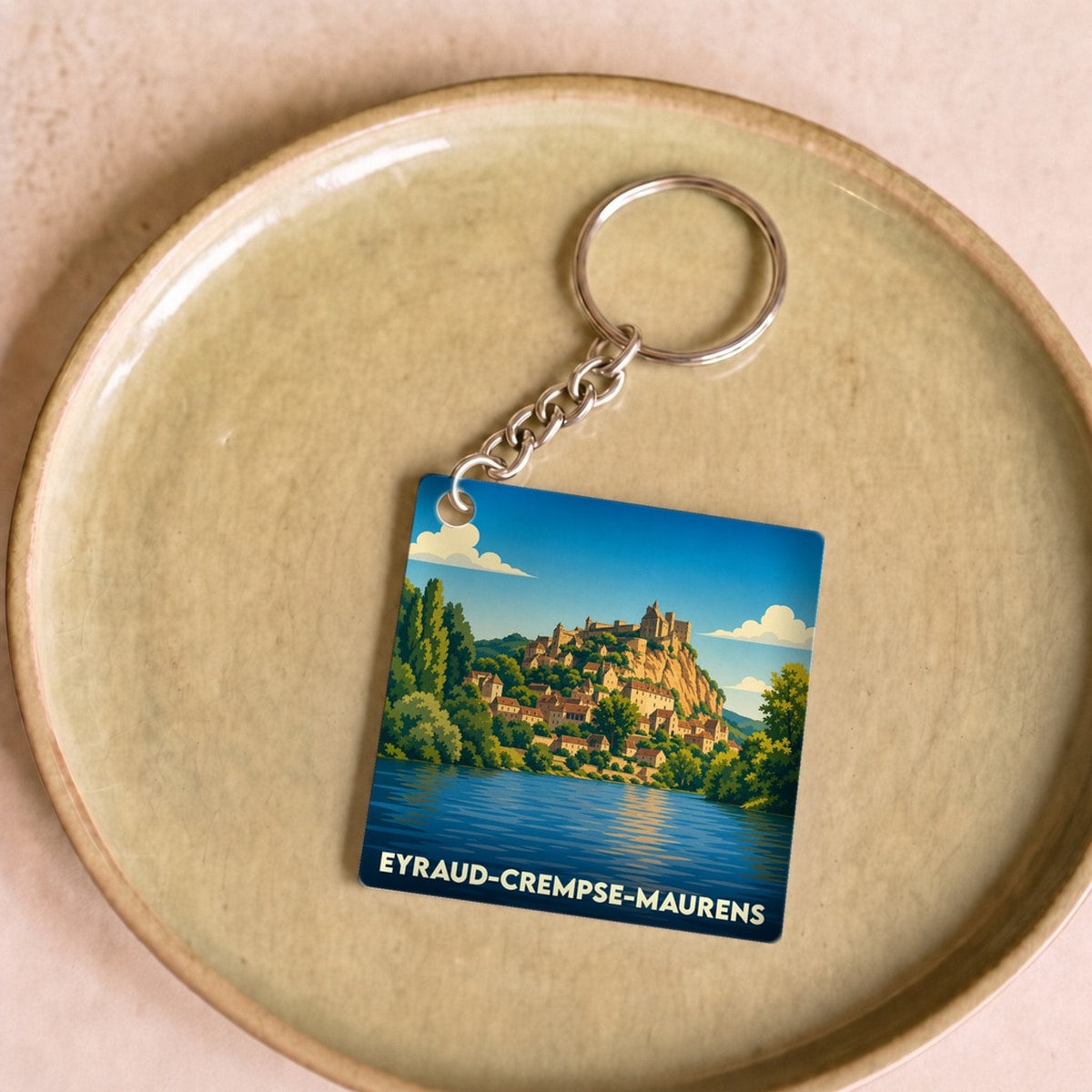 Porte-clés souvenir de la ville de Eyraud-Crempse-Maurens avec une illustration stylisée d'un village surplombant l'eau.