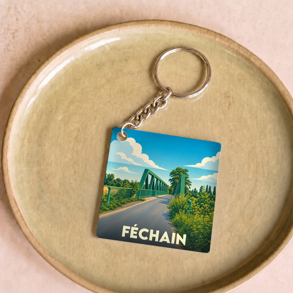 Porte-clés souvenir de la ville de Féchain avec une illustration stylisée d'un pont vert sous un ciel bleu.