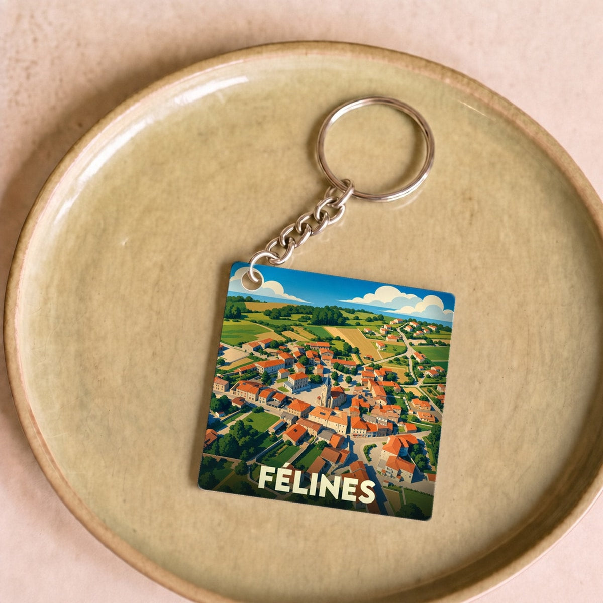 Porte-clés souvenir de la ville de Félines avec une illustration stylisée d'une vue aérienne du village.