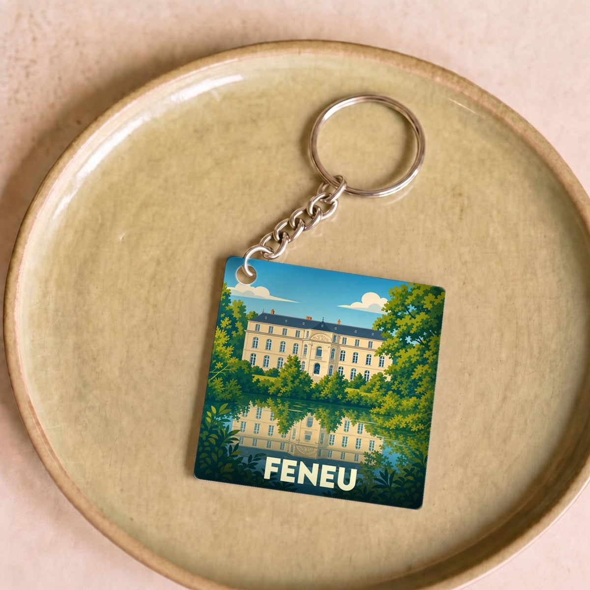 Porte-clés souvenir de la ville de Feneu avec une illustration stylisée d'un château se reflétant dans l'eau.