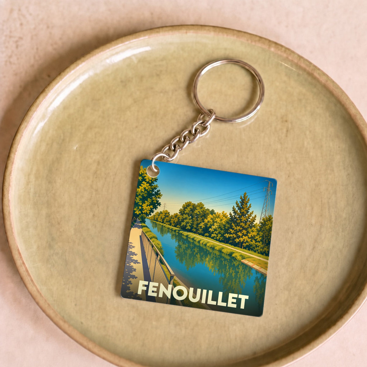 Porte-clés souvenir de la ville de Fenouillet avec une illustration stylisée d'un canal bordé d'arbres.