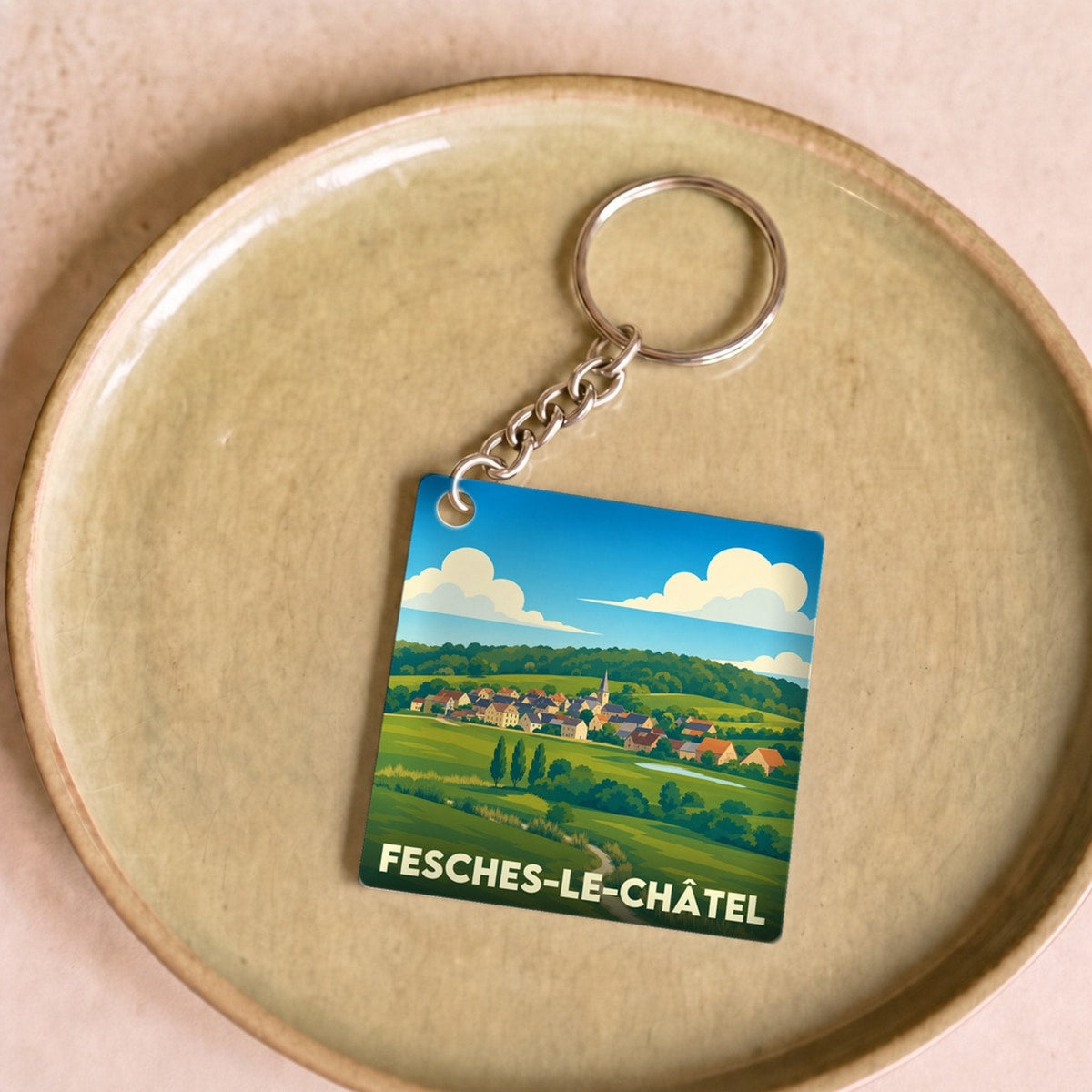 Porte-clés souvenir de la ville de Fesches-le-Châtel avec une illustration stylisée de son paysage rural.