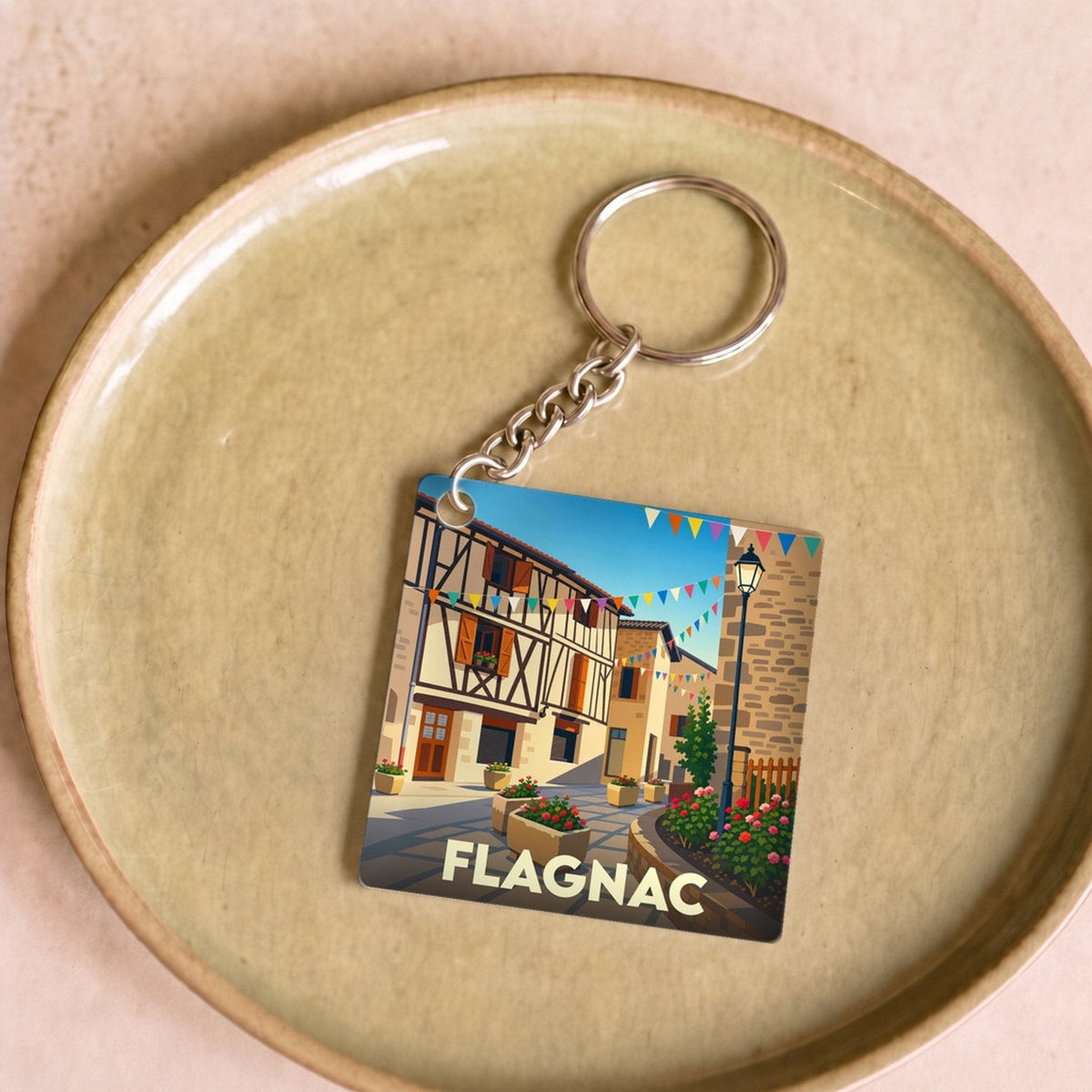 Porte-clés souvenir de la ville de Flagnac avec une illustration stylisée d'une rue pittoresque.