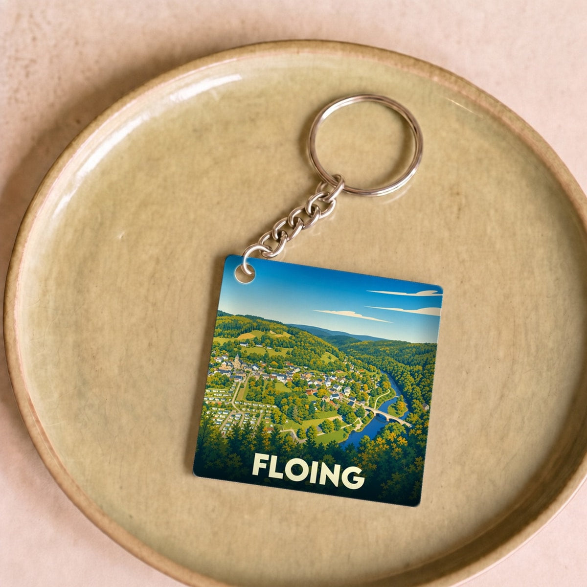 Porte-clés souvenir de la ville de Floing avec une illustration stylisée d'un paysage de vallée.