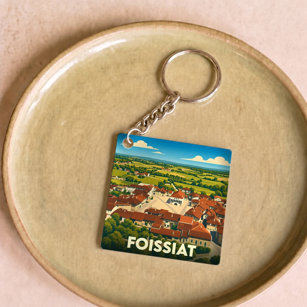 Porte-clés souvenir de la ville de Foissiat avec une illustration stylisée d'un paysage de village.