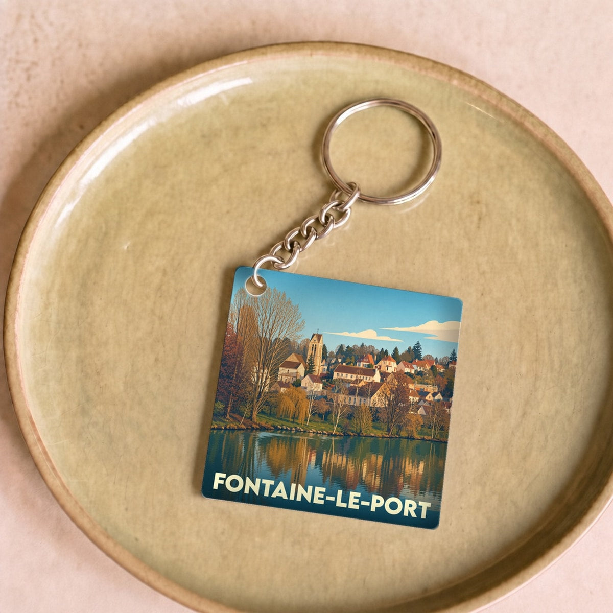 Porte-clés souvenir de la ville de Fontaine-le-Port avec une illustration stylisée d'un paysage de bord d'eau.