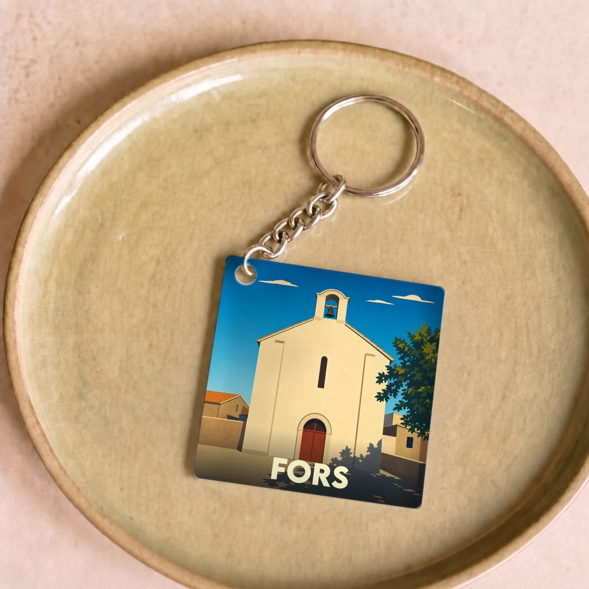 Porte-clés souvenir de la ville de Fors avec une illustration stylisée de son église sous un ciel bleu.
