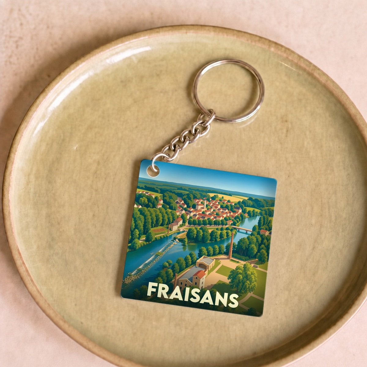 Porte-clés souvenir de la ville de Fraisans avec une illustration stylisée d'un paysage urbain au bord de l'eau.
