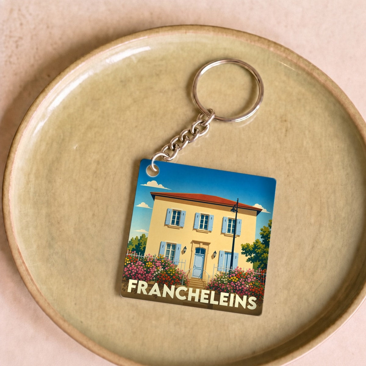 Porte-clés souvenir de la ville de Francheleins avec une illustration stylisée d'une maison ensoleillée.