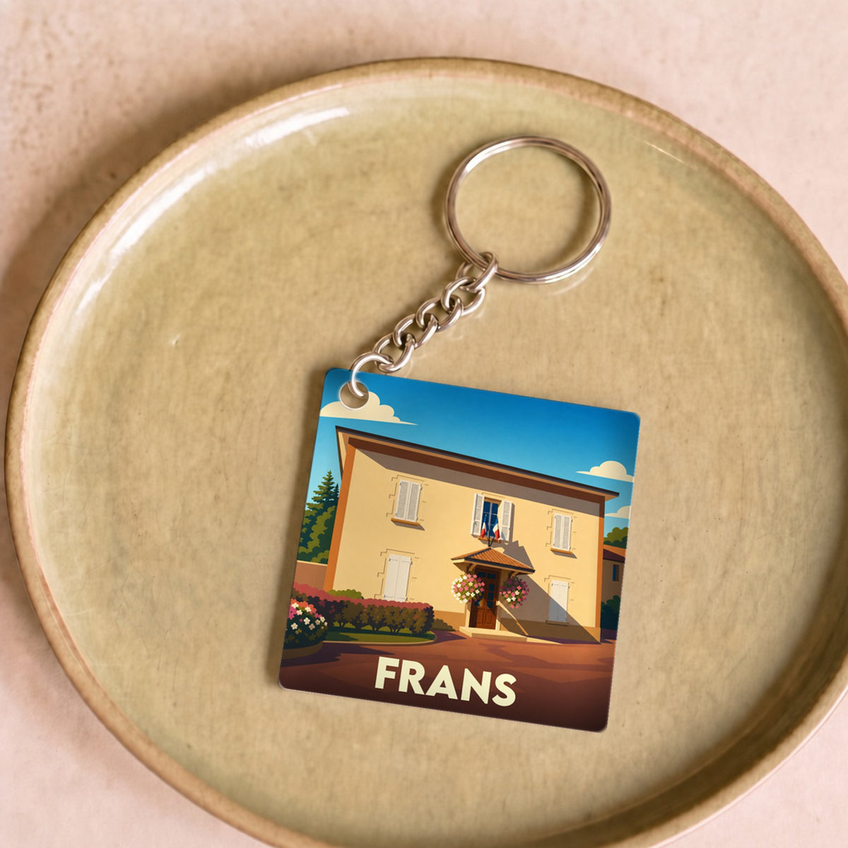 Porte-clés souvenir de la ville de Frans avec une illustration stylisée d'une maison ensoleillée.
