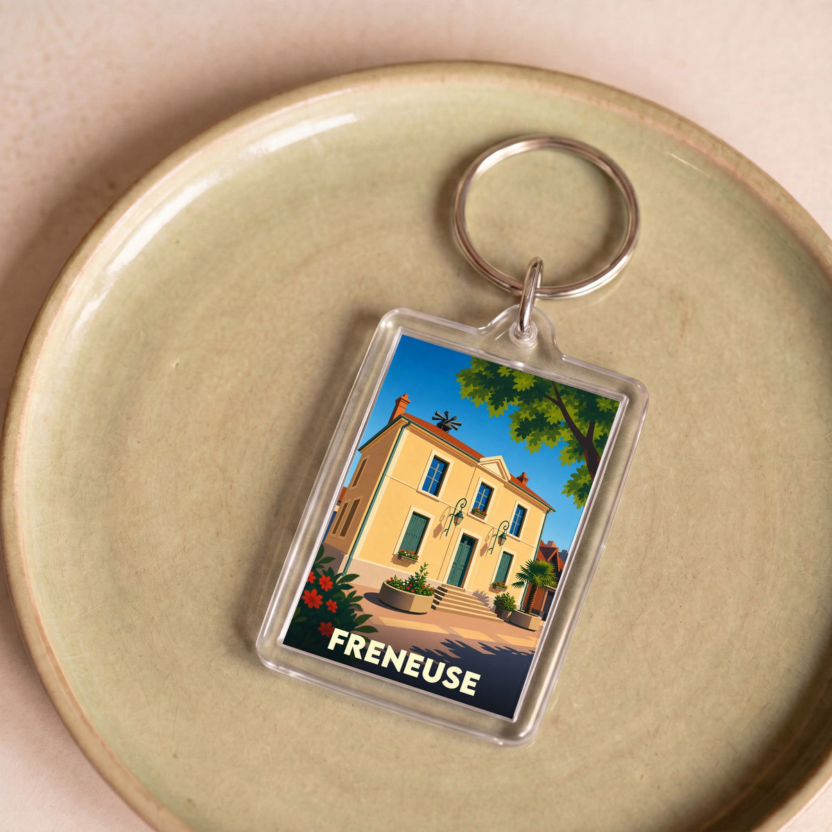Porte-clés souvenir de la ville de Freneuse avec une illustration stylisée d'un bâtiment ensoleillé.