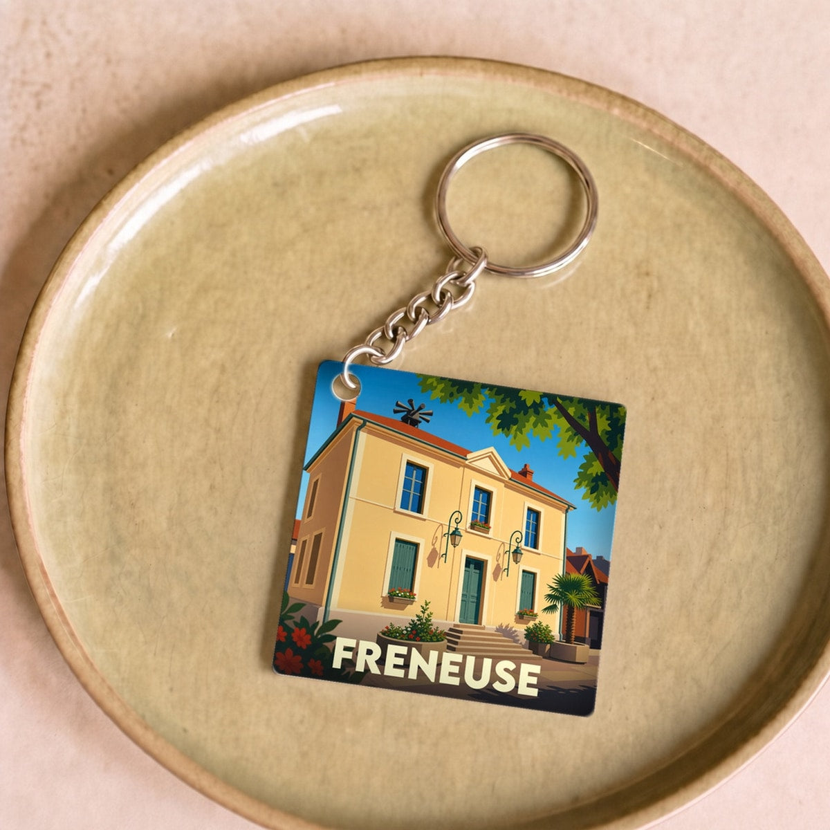 Porte-clés souvenir de la ville de Freneuse avec une illustration stylisée d'un bâtiment ensoleillé.