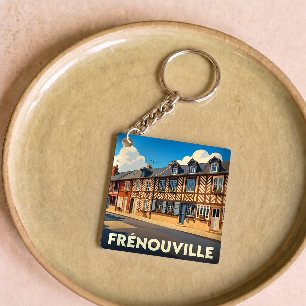 Porte-clés souvenir de la ville de Frénouville avec une illustration stylisée de maisons à colombages.
