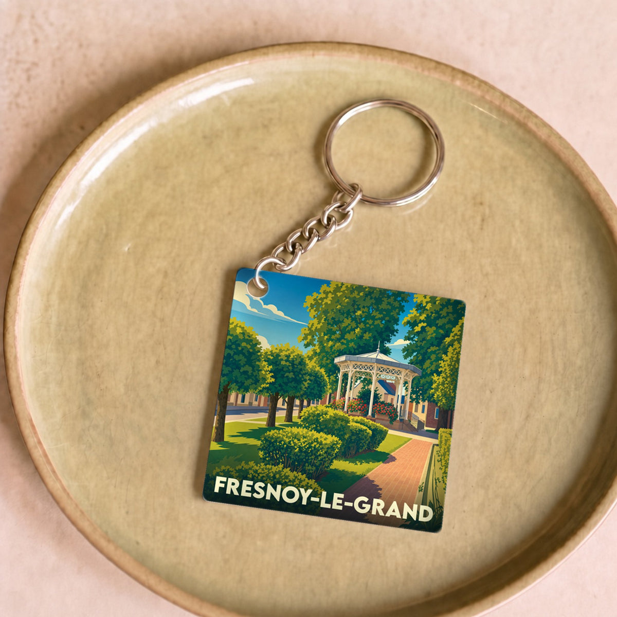 Porte-clés souvenir de la ville de Fresnoy-le-Grand avec une illustration stylisée d'un parc et son kiosque.