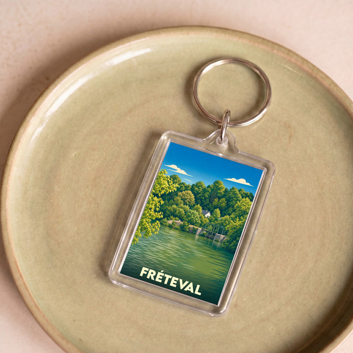 Porte-clés souvenir de la ville de Fréteval avec une illustration stylisée d'un paysage de rivière.