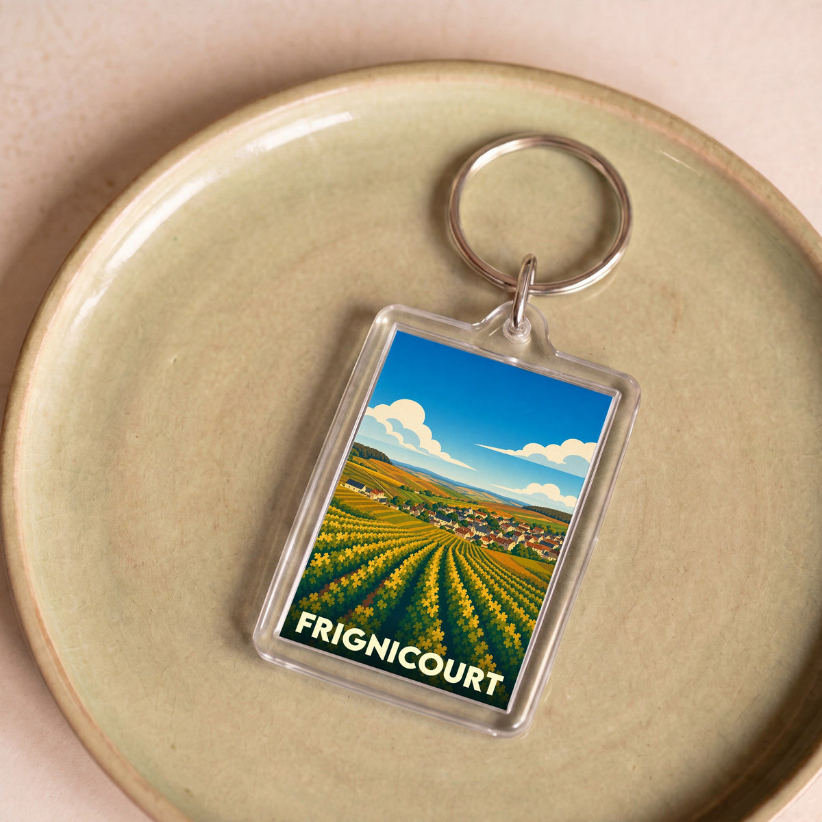 Porte-clés souvenir de la ville de Frignicourt avec une illustration stylisée de paysages vallonnés.