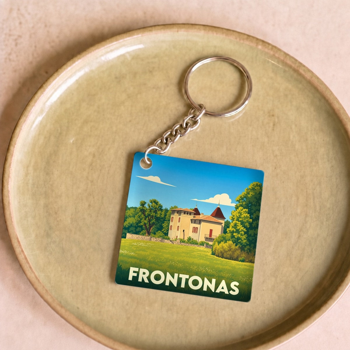 Porte-clés souvenir de la ville de Frontonas avec une illustration stylisée d'un château dans un paysage verdoyant.